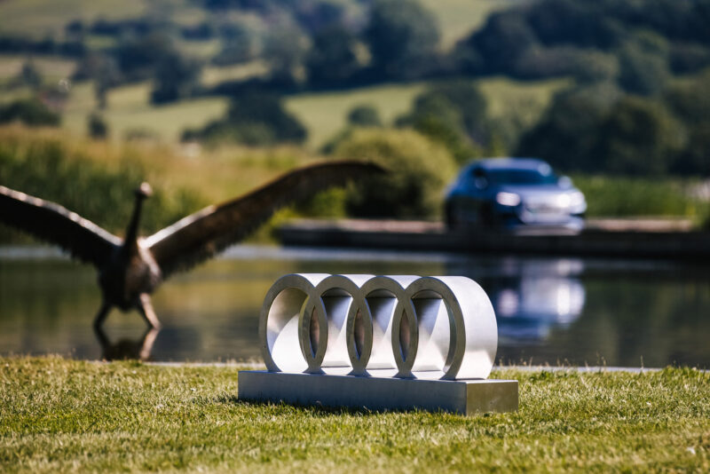 Audi Car driving past a lake with a bird statue